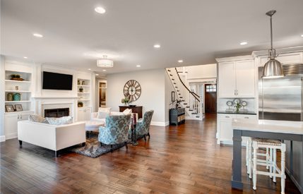 Living room with hardwood floors, white furniture, a fireplace, a television, shelves with photo frames, a clock on the wall